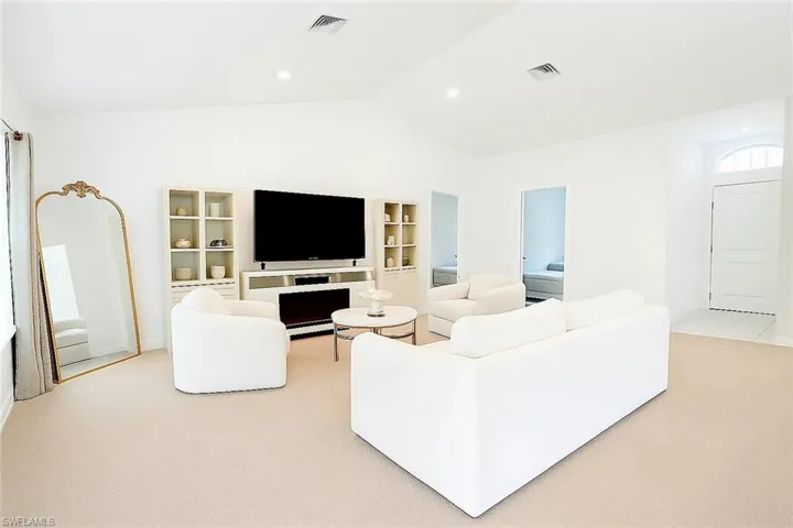 Living room with vaulted ceiling, built in shelves, and light carpet