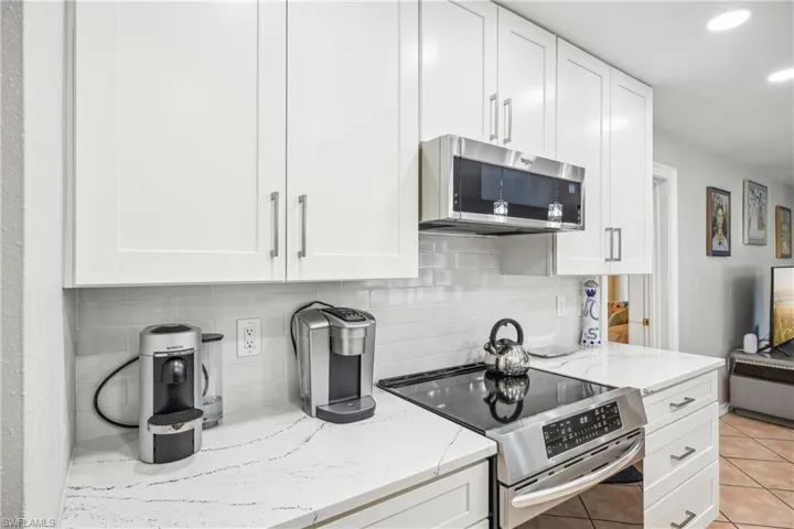 Kitchen featuring white cabinets, light stone countertops, light tile patterned floors, and stainless steel appliances