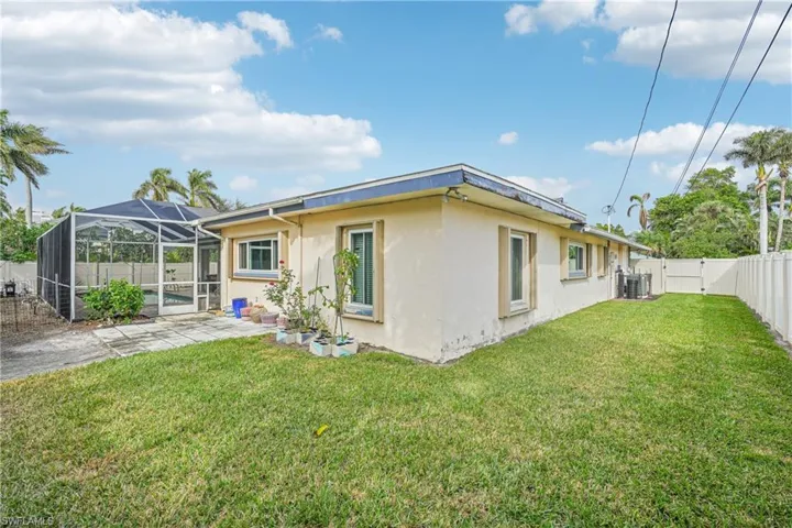 Back of property with a lanai, central air condition unit, and a lawn