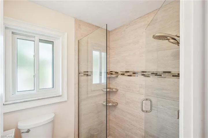 Bathroom with a healthy amount of sunlight, toilet, and a shower with shower door