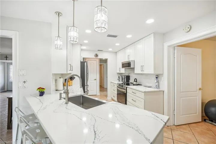 Kitchen featuring backsplash, sink, hanging light fixtures, appliances with stainless steel finishes, and white cabinetry