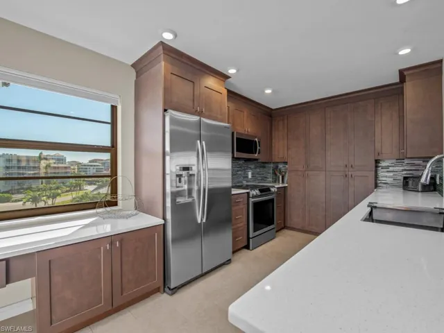 Kitchen with light stone countertops, appliances with stainless steel finishes, backsplash, sink, and light tile patterned flooring