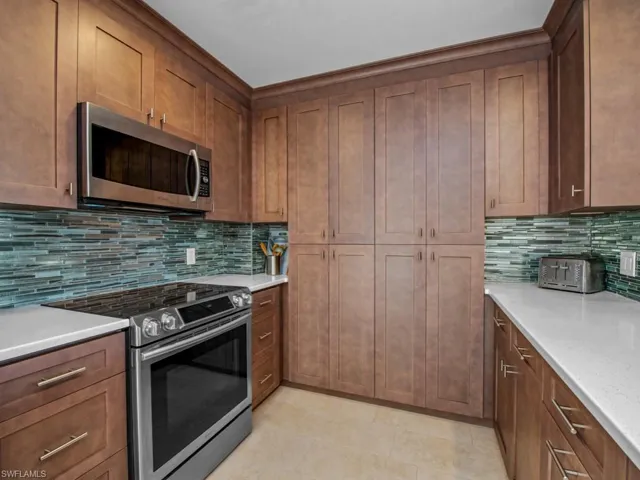 Kitchen with tasteful backsplash, light stone countertops, light tile patterned floors, and appliances with stainless steel finishes