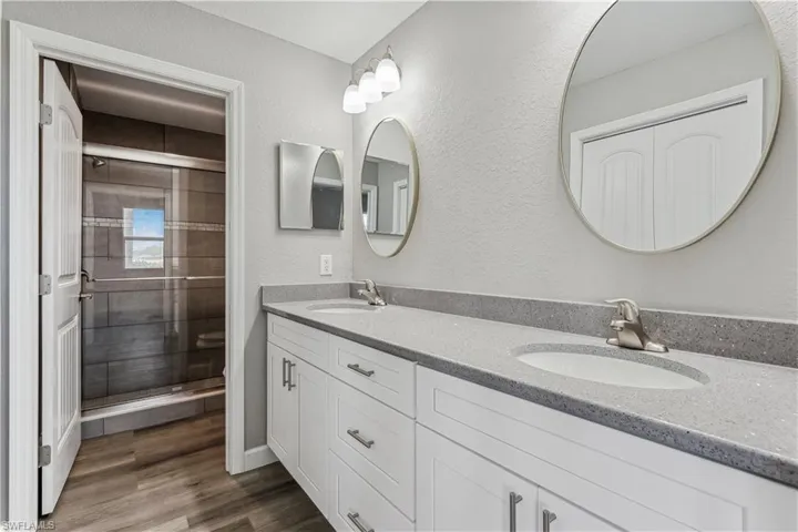 Bathroom with double sink vanity, LVP floors, and a shower with door