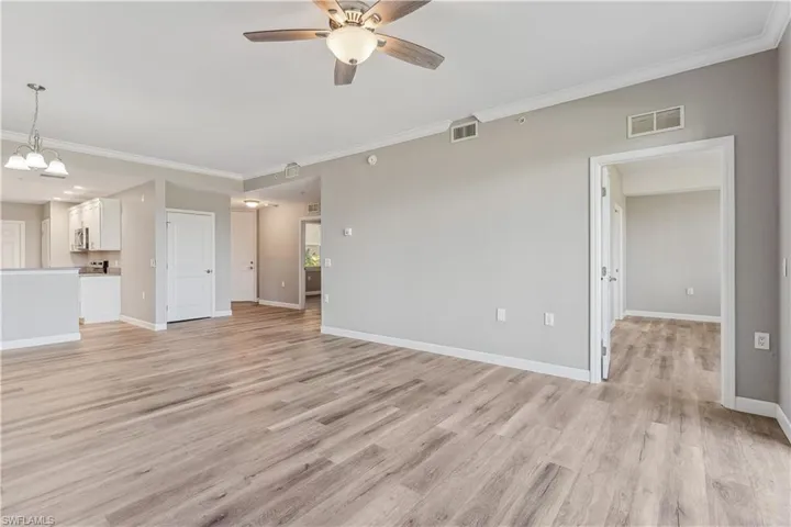 Unfurnished living room featuring ceiling fan with notable chandelier, LVP style floors, and ornamental molding