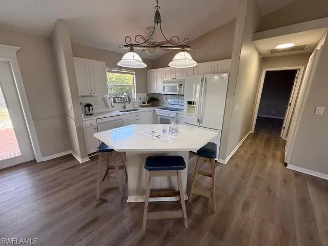 Kitchen featuring white appliances, white cabinetry, dark wood-style floors, light countertops, and vaulted ceiling