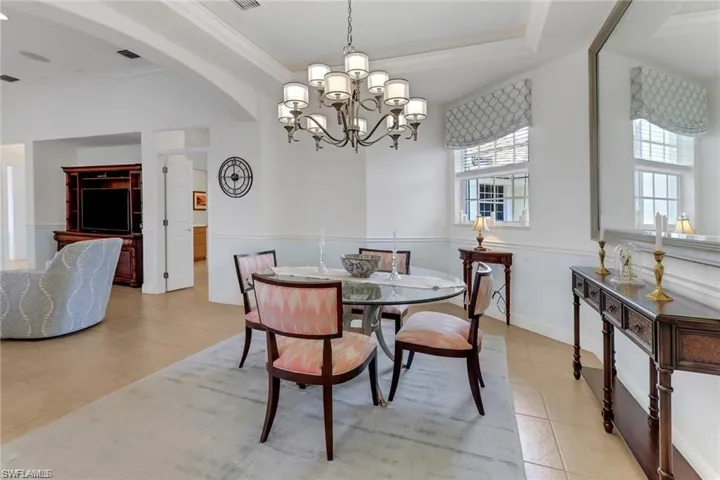 Tiled dining area featuring a raised ceiling, an inviting chandelier, and ornamental molding