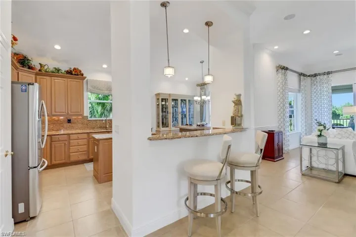 Kitchen featuring backsplash, light stone counters, stainless steel refrigerator, light tile patterned floors, and kitchen peninsula