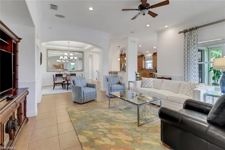 Tiled living room featuring crown molding and ceiling fan with notable chandelier