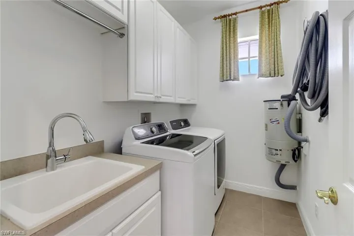 Laundry room featuring sink, washing machine and clothes dryer, cabinets, and light tile patterned floors