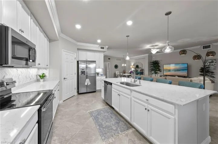 Kitchen featuring a large island, large pantry, ample counter area, beautiful custom backsplash, stainless appliances, and decorative light fixtures