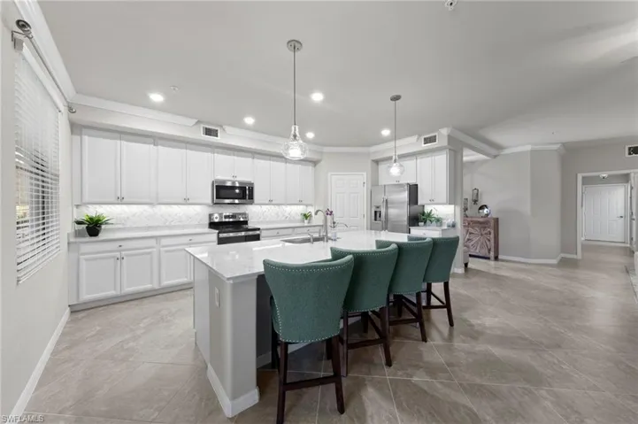 Kitchen featuring a large island, beautiful custom backsplash, stainless appliances, and decorative light fixtures
