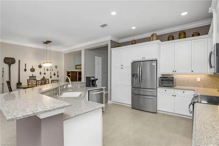 Kitchen featuring stainless steel appliances, a center island with sink, sink, light stone countertops, and decorative light fixtures