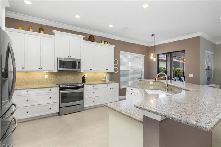 Kitchen with white cabinetry, sink, appliances with stainless steel finishes, an island with sink, and pendant lighting