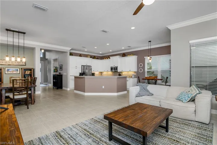 Living room featuring ceiling fan with notable chandelier, light tile patterned floors, and crown molding