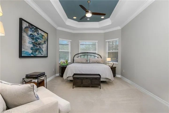 Carpeted bedroom featuring ornamental molding, ceiling fan, and a raised ceiling