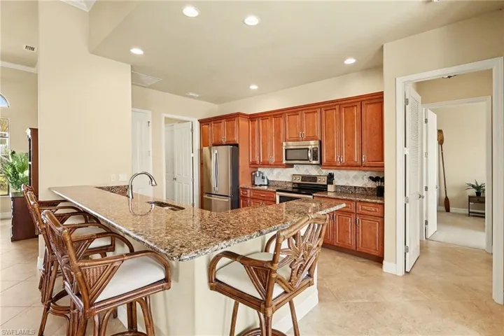 Kitchen with light stone countertops, a kitchen bar, wood finish soft touch cabinets, and recessed lighting.