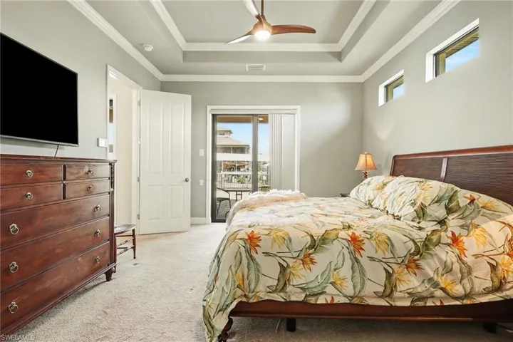 Carpeted master bedroom featuring access to exterior, a ceiling fan, a tray ceiling, and ornamental molding.