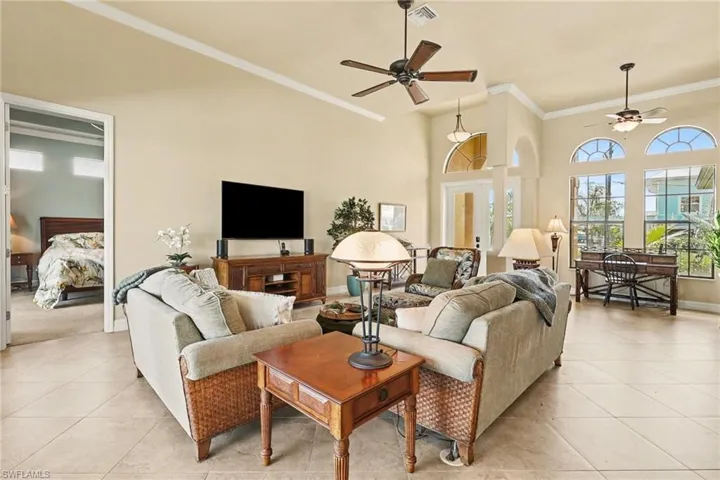 Living room with crown molding, ceiling fan, show casing the high ceilings, and luxury tile patterned flooring.
