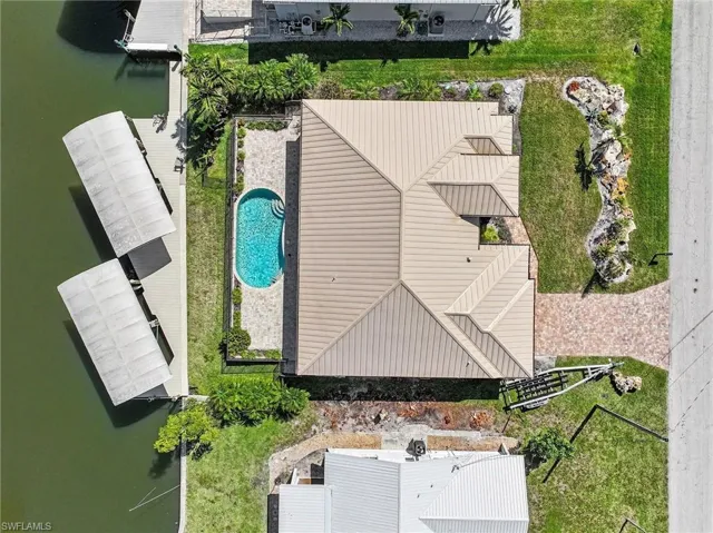 Bird's eye view of a pool area, covered docks, metal roof, and landscaped yard.