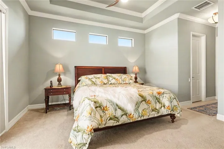 Bedroom featuring a tray ceiling, light carpet, crown molding, and a ceiling fan.