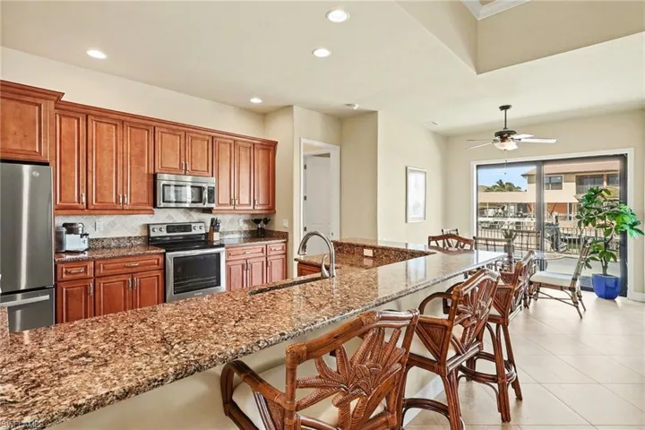 Kitchen with a breakfast bar area, stainless steel appliances, wood finish soft touch cabinets, quartz counters, and decorative backsplash.