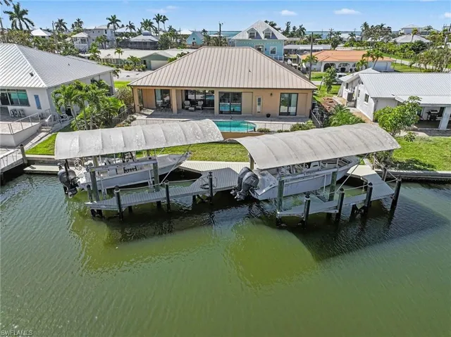 Dock area with boat lift, an outdoor pool, a residential view, and a patio area