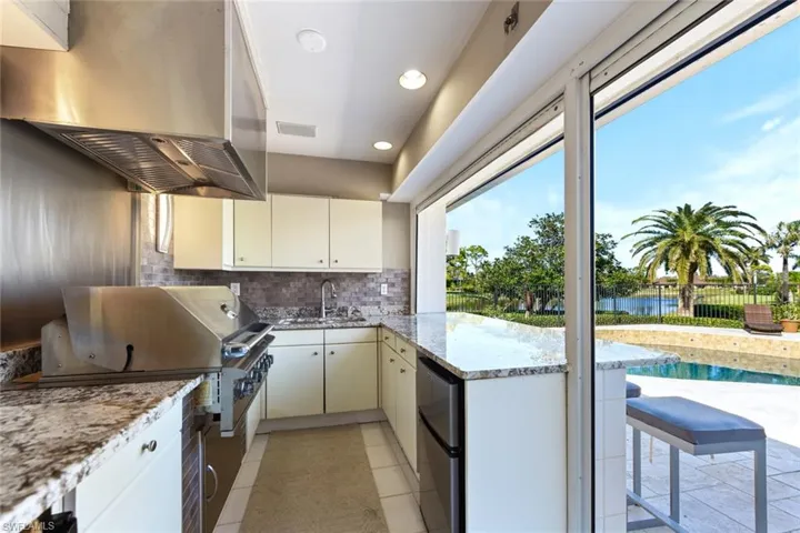 Outdoor kitchen with ventilation hood, two refrigerators, a water view, double sink, and light tile floors