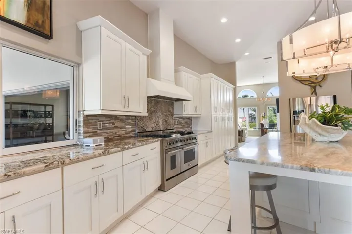 Kitchen featuring decorative backsplash, custom range hood, stainless steel appliances, white cabinets, and hanging light fixtures