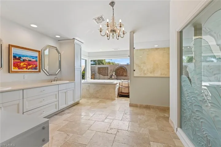 Bathroom with double vanity, tiled bath, and an inviting chandelier
