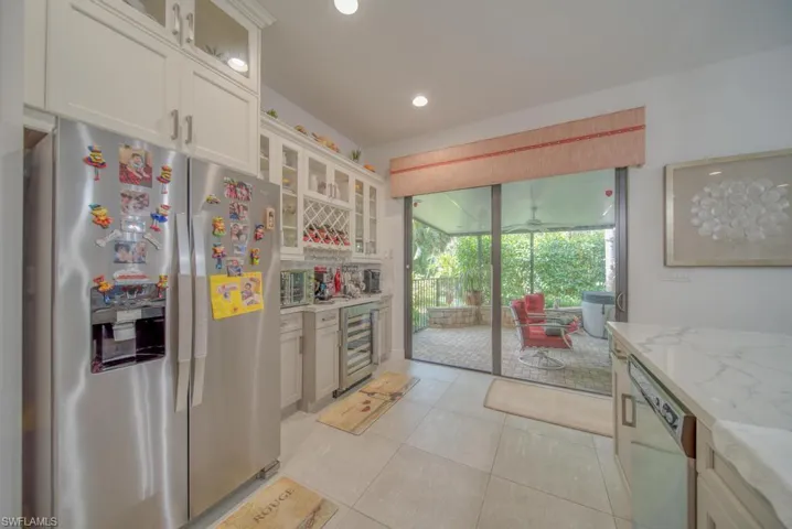 Kitchen with white cabinets, dishwasher, stainless steel refrigerator with ice dispenser, and light stone counters