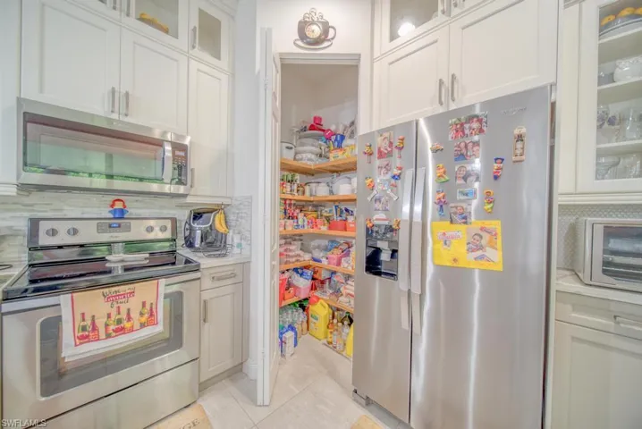 Kitchen with appliances with stainless steel finishes, white cabinets, decorative backsplash, and light tile patterned floors