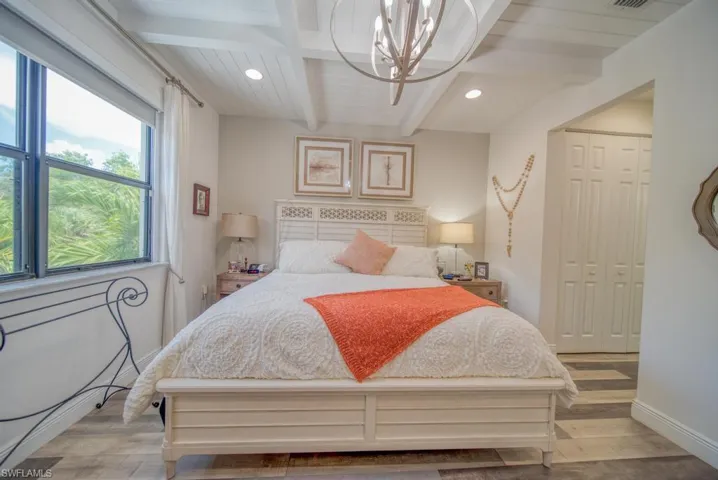 Bedroom featuring light wood-type flooring, a closet, a notable chandelier, and beam ceiling