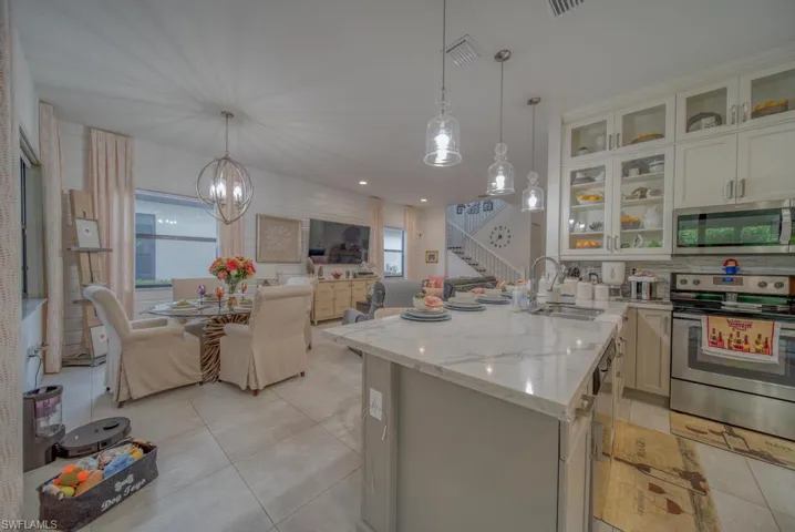 Kitchen with hanging light fixtures, stainless steel appliances, light stone countertops, white cabinets, and sink