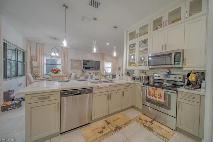 Kitchen featuring appliances with stainless steel finishes, hanging light fixtures, light stone countertops, sink, and a healthy amount of sunlight