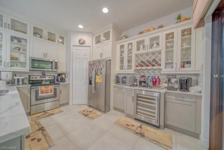 Kitchen featuring white cabinetry, stainless steel appliances, backsplash, light stone counters, and beverage cooler