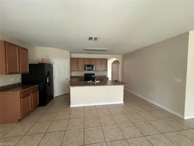 Kitchen with light tile patterned floors, sink, black appliances, and an island with sink