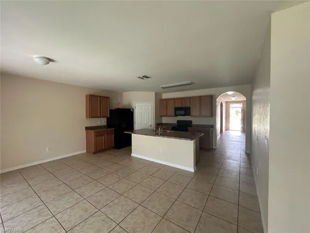 Kitchen featuring arched walkways, light tile patterned floors, dark countertops, visible vents, and black appliances