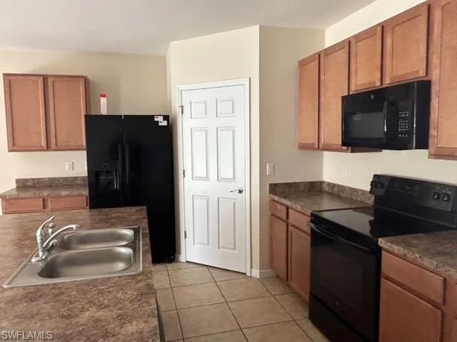 Kitchen with black appliances, brown cabinetry, light tile patterned flooring, and a sink