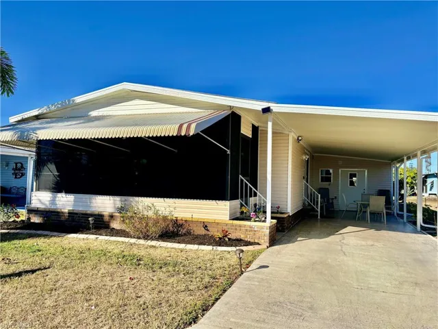 Manufactured / mobile home featuring concrete driveway, a carport, a front yard, covered porch, and entry steps