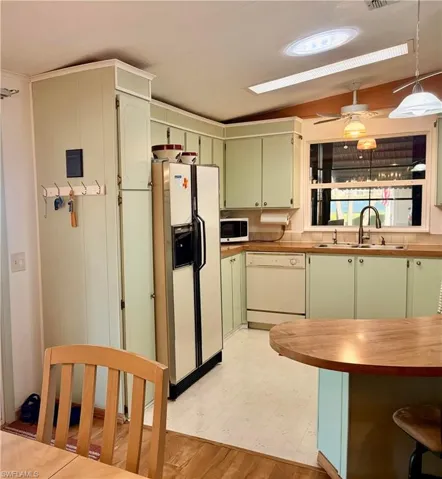 Kitchen featuring green cabinets, white appliances, ceiling fan, pendant lighting, and light flooring