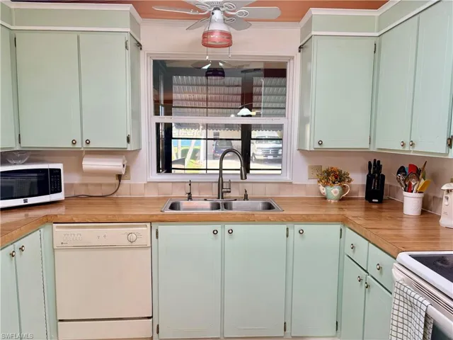 Two tone kitchen with white appliances, light countertops, ceiling fan, and two tone cabinetry