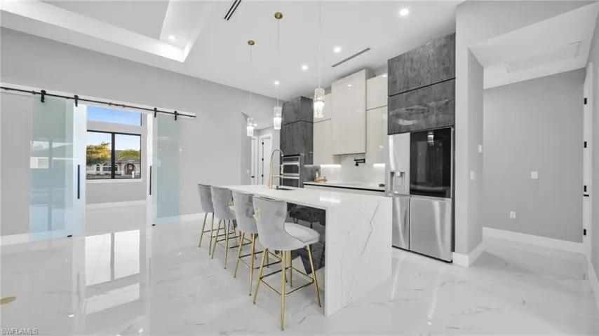 Kitchen with modern cabinets, dual tone cabinetry, stainless steel fridge with ice dispenser, pendant lighting, and a center island with sink