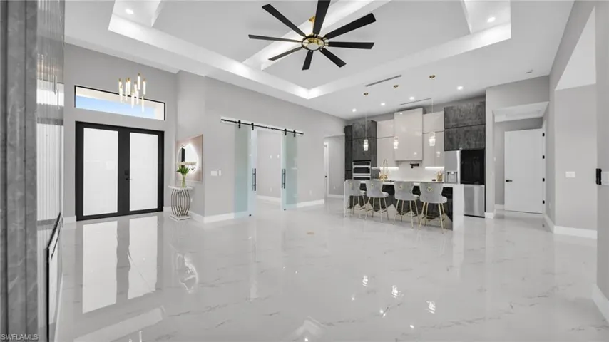 Unfurnished living room featuring a barn door, light marble finish flooring, ceiling fan, recessed lighting, and a high tray ceiling