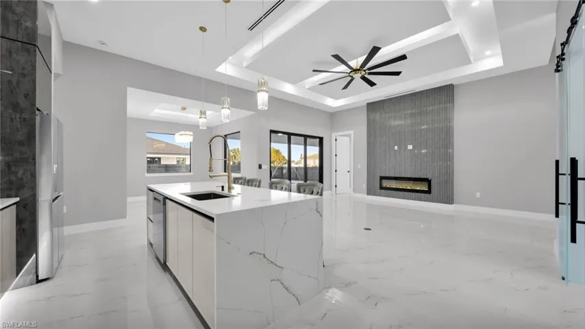 Kitchen featuring modern cabinets, white cabinetry, a tray ceiling, light stone counters, and decorative light fixtures