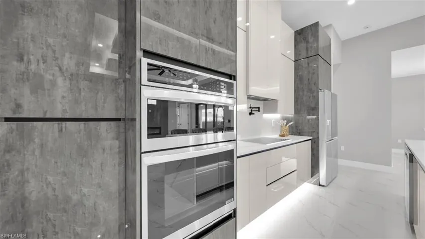 Two tone kitchen with modern cabinets, stainless steel double oven, dual tone cabinetry, freestanding refrigerator, and light marble finish floors
