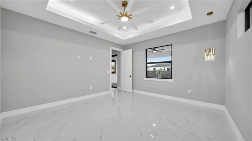 Spare room featuring a raised ceiling, hanging lights, a ceiling fan, and light marble finish floors