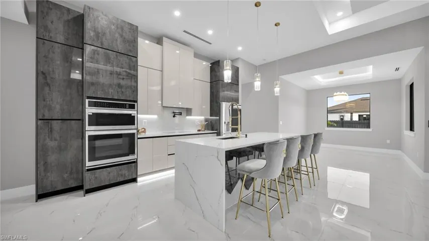 Kitchen featuring dual tone cabinets, modern cabinets, decorative light fixtures, and light marble finish flooring