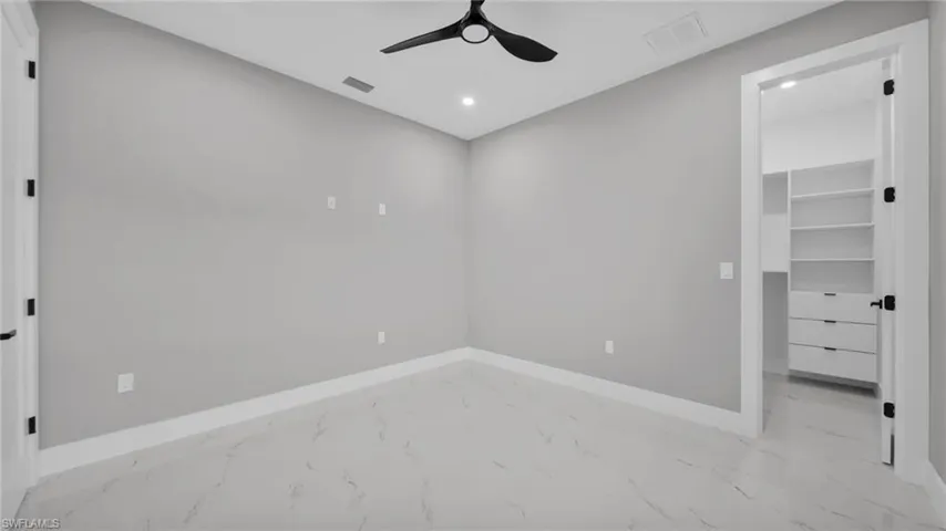 Unfurnished bedroom with a spacious closet, marble look tiles, recessed lighting, and ceiling fan