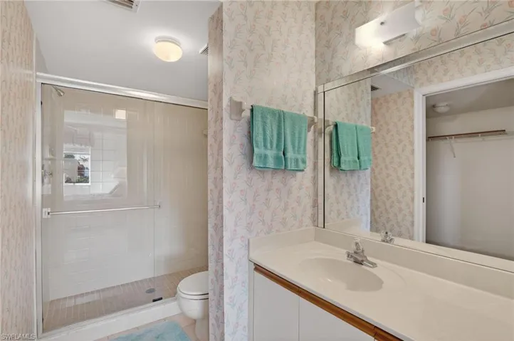Bathroom featuring vanity, wallpapered walls, a walk in closet, a stall shower, and light tile patterned flooring